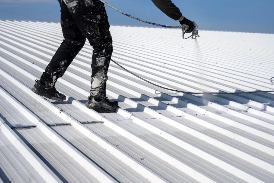 Worker painting metal roof white.
